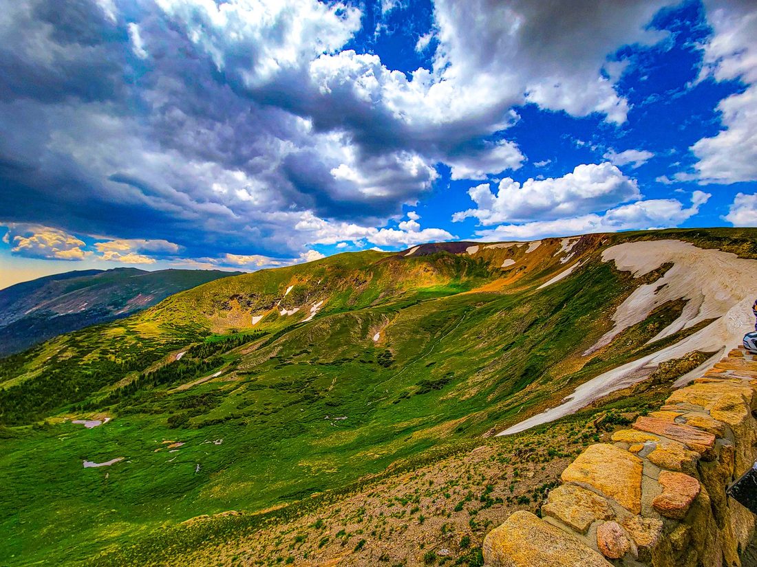 Green high mountain ridge with a lingering snow patch under big summer clouds