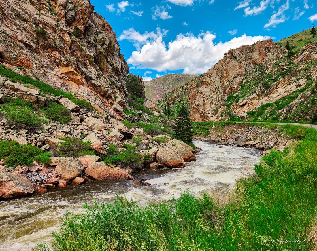 A fast river running through a rocky canyon with green grass and rugged cliffs
