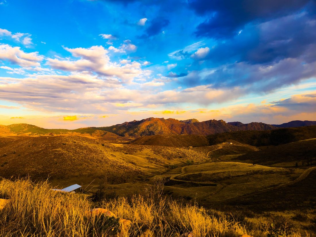 Rolling grassy hills and a rocky ridge stretch toward the horizon under a wide cloudy sky