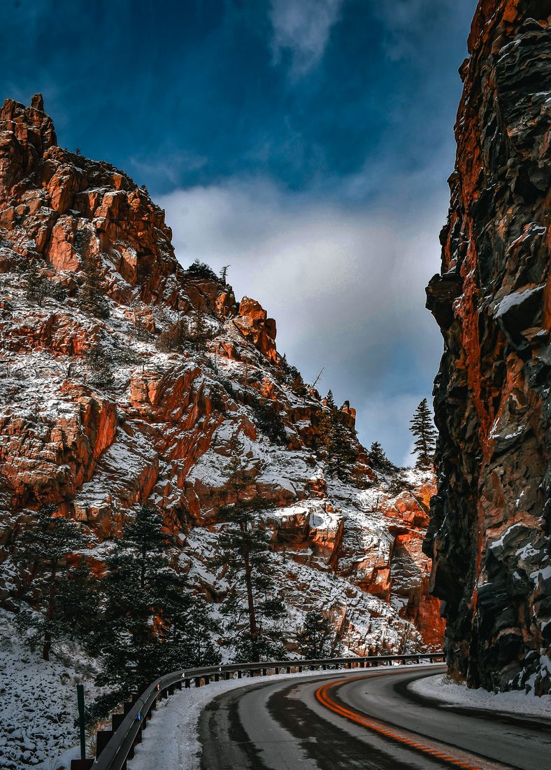 A curving road winding through a snowy canyon between red rock cliffs under a dark sky