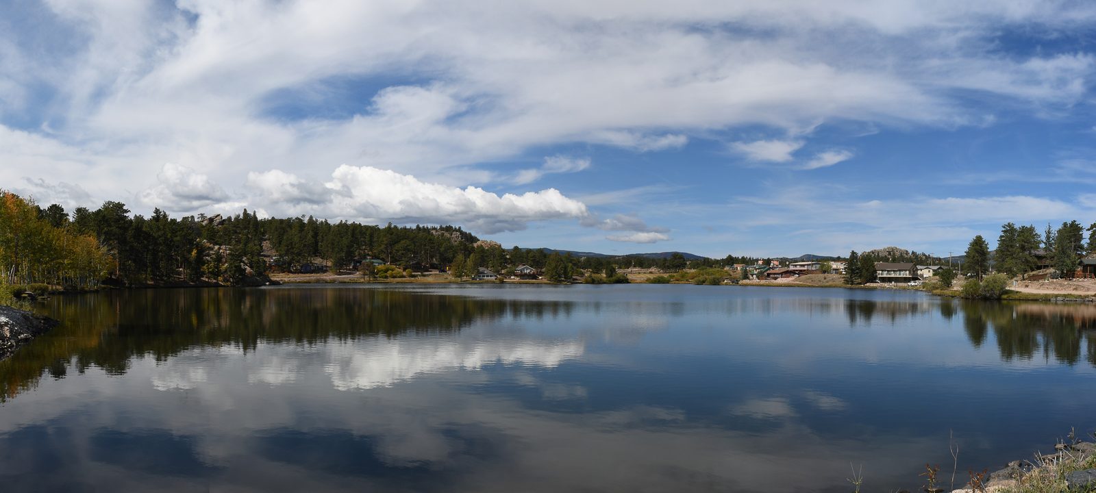 A calm mountain lake reflecting the clouds beside a small rural mountain town ringed by pines