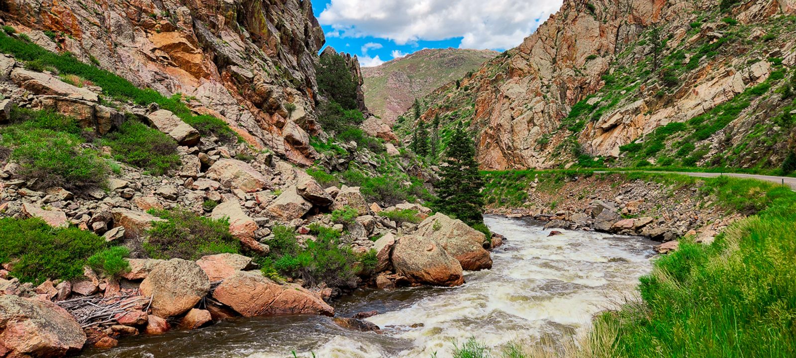 A whitewater river rushing through a steep rocky mountain canyon beside a winding rural road