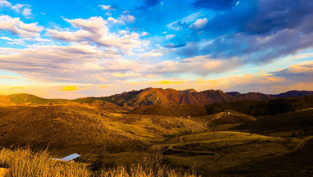 Rolling grassy hills and a rocky ridge stretch toward the horizon under a wide cloudy sky